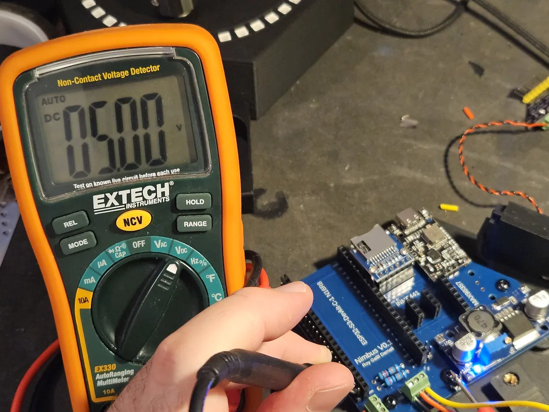 An Extech EX330 multimeter reading 05.00 V DC beside the Nimbus board's DC-DC converter