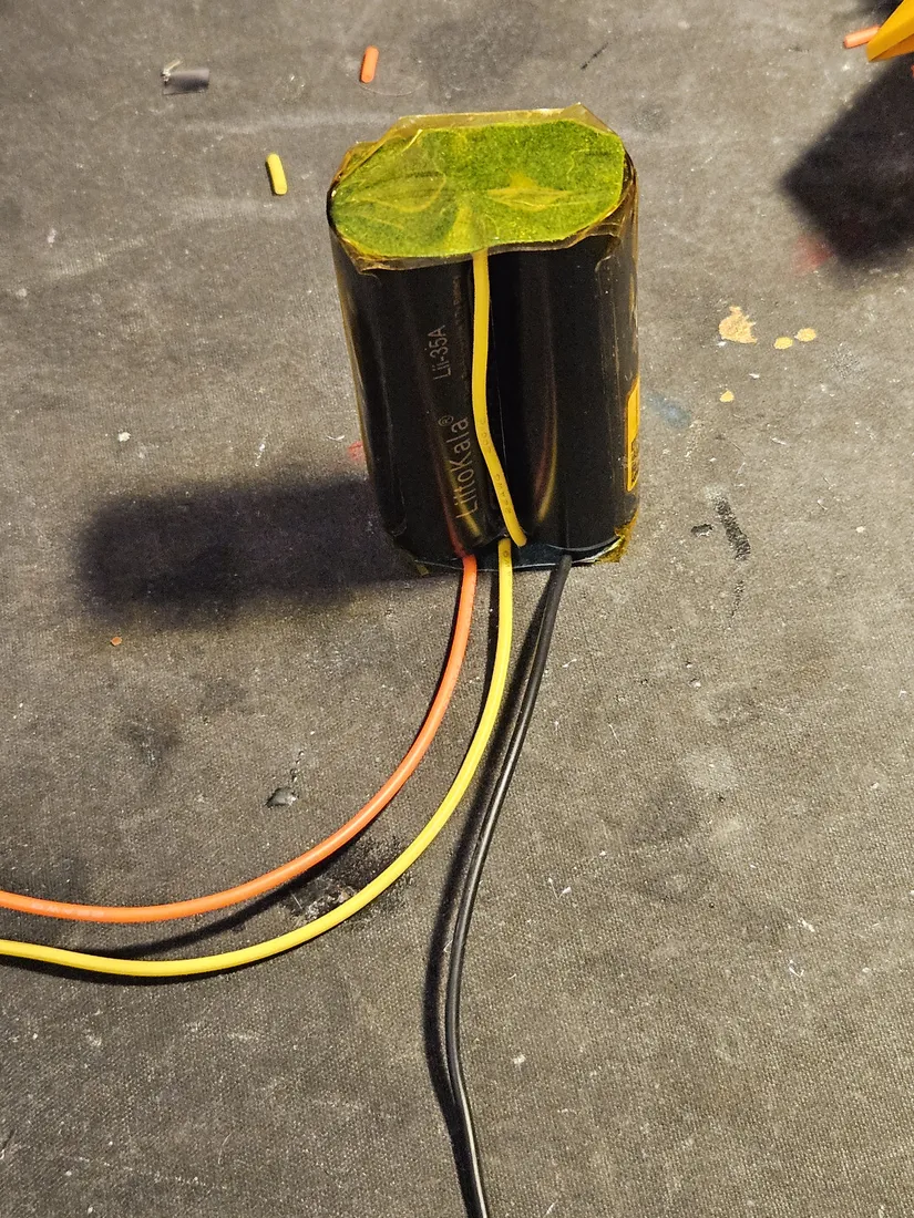 Two 18650 cells taped side by side with a translucent fish-paper insulator covering the terminal ends, pack leads exiting the bottom
