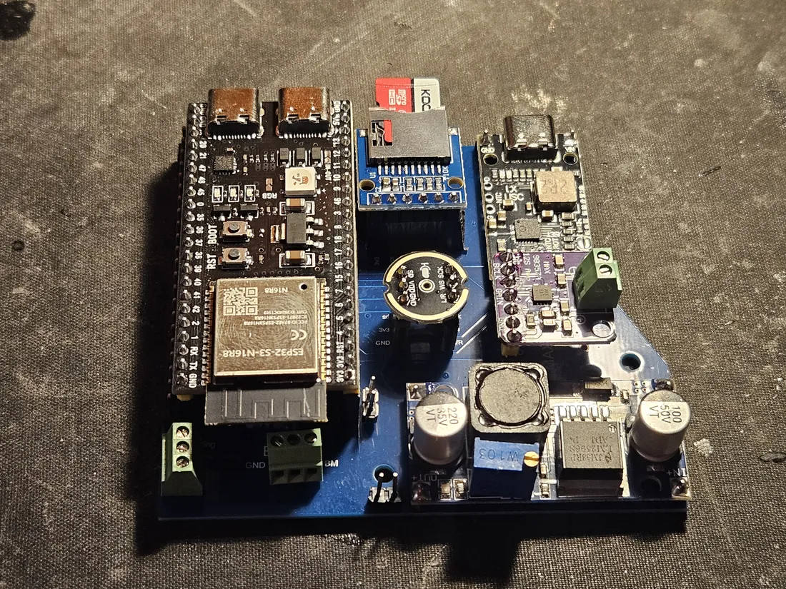 The same electronics stack at an angle, the blue Nimbus PCB carrying all modules and resting on the black printed standoff frame, green screw terminals along the front edge