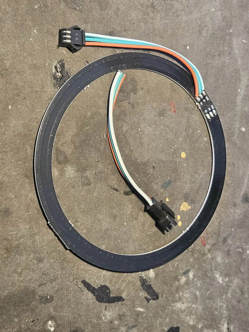 The ring opened at one point where the single power ribbon bridging its ends has been cut, the loop no longer continuous, the pigtail and every pixel left intact