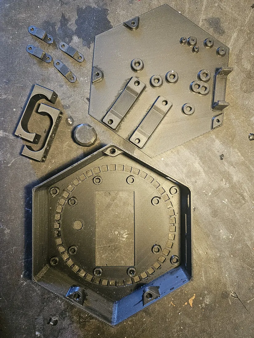Full set of black 3D-printed enclosure parts: top plate, bottom tub, small clip brackets, an S-logo bracket, and a hex plug