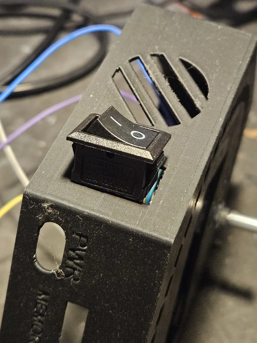 Black rocker switch pressed into a rectangular cutout in the printed case top, next to vent slots, above an embossed PWR label