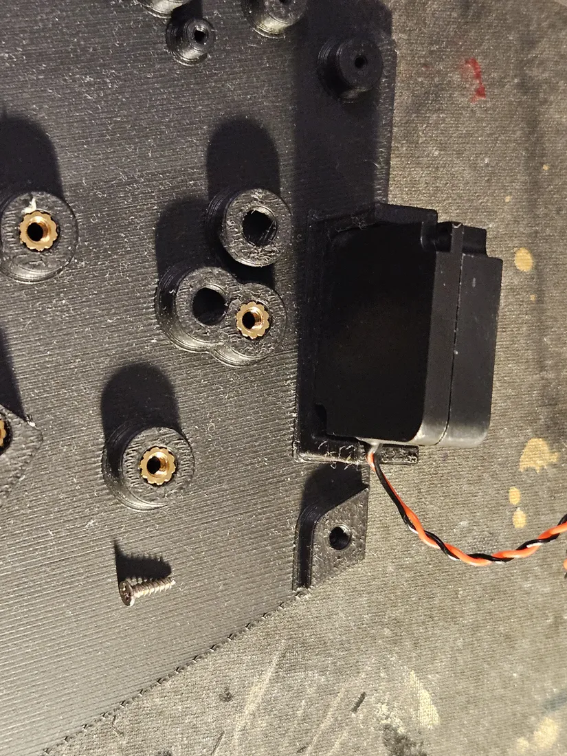 Speaker seated in a printed pocket beside a cluster of brass heat-set inserts, with a self-tapping screw staged nearby